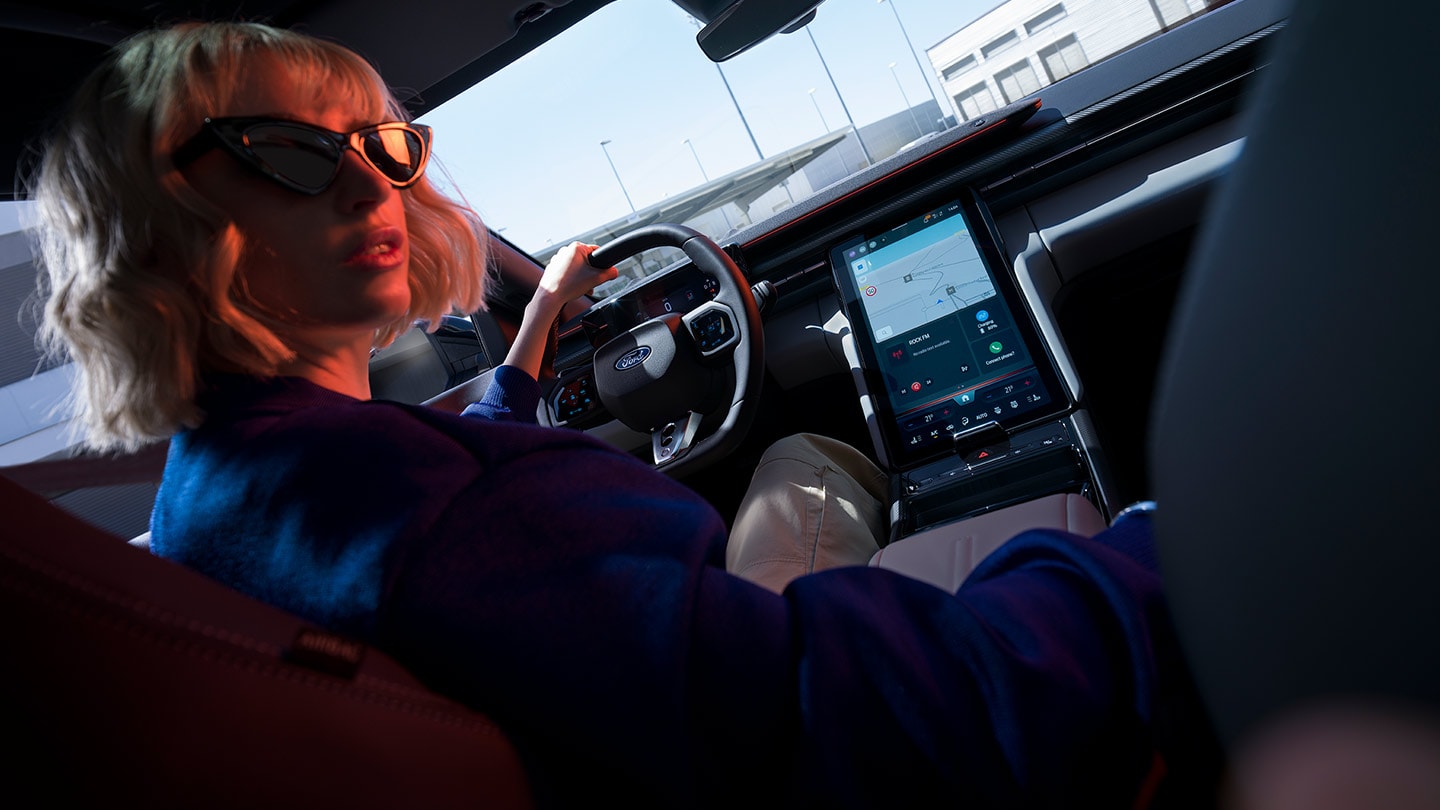 Vrouw die de nieuwe Ford Capri® bestuurt met zicht op het stuurwiel, het dashboard en het grote SYNC® Move-touchscreen.