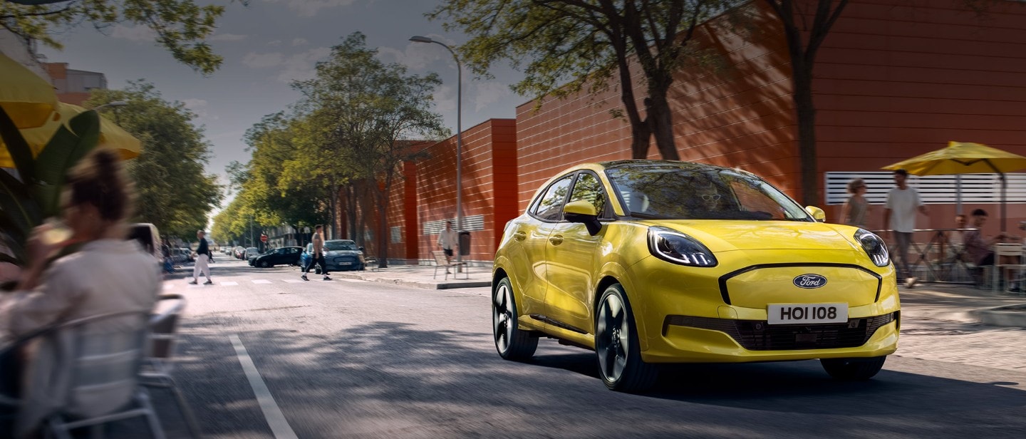 Vooraanzicht van een gele elektrische Ford Puma Gen-E® die op een stadsweg rijdt.